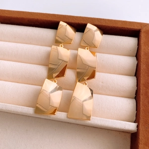 Macro view of gold plated square tassel earrings displayed in a luxury beige jewelry box