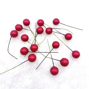 Close-up of bright red artificial berries with wire stems on white plush background