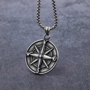 Macro detail of vintage silver compass pendant with NESW engraving on stone background