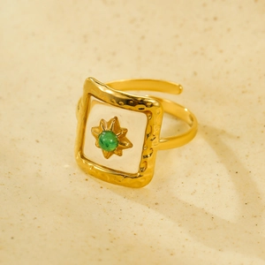 Vintage adjustable gold ring with green gemstone in a starburst setting on white enamel
