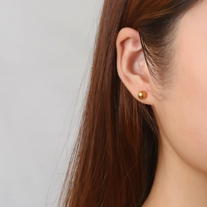 Close-up of minimalist polished gold sphere stud earring worn by a model in detail view