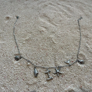 Silver ocean themed shell necklace with pearl charms on sandy texture background
