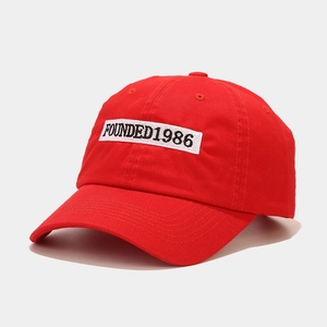Detailed close-up of red cotton baseball cap featuring Founded 1986 white patch embroidery