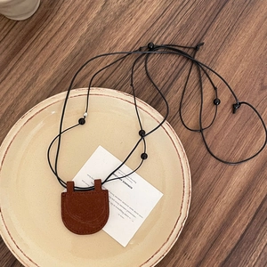Vintage brown suede mini bag necklace displayed on a ceramic tray over dark wood texture