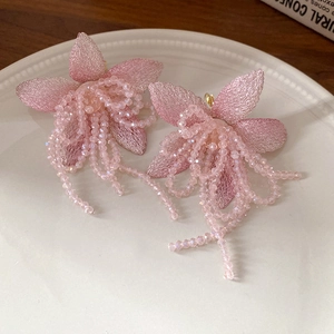 Detail of pink tulle flower earrings with crystal beads and gold tassels on a ceramic tray