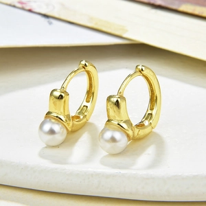 Elegant gold huggie earrings with round white pearls on a minimalist stone display stand