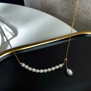 Detail of 14K gold-filled necklace featuring white round pearls and a drop-shaped pendant