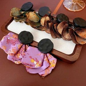 Retro brocade floral earrings with black textured center on elegant wooden tray display