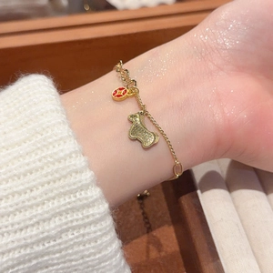 Detail of a gold bracelet with zircon pony and red round pendants on a model's wrist