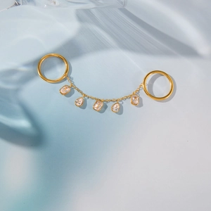 Vue macro de bagues doubles en acier doré avec chaîne à pampilles en zircon et reflets d'eau
