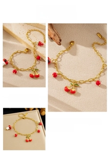 Détails d'un bracelet doré avec des breloques en émail en forme de cerise et fraise