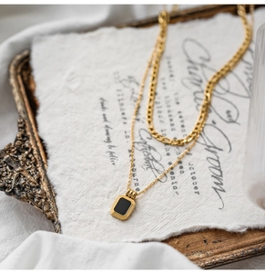 Close-up of double-layer gold necklace with black rectangle pendant on vintage paper