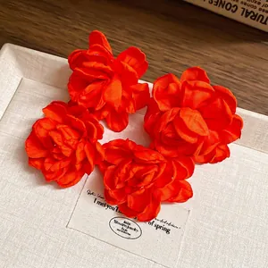 Elegant set of four red satin fabric flower earrings displayed on a textured beige tray
