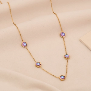 Dettaglio collana dorata con cinque ciondoli a fiore viola su sfondo beige morbido