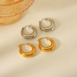 Polished gold and silver hollow geometric hoop earrings on a minimalist ivory surface