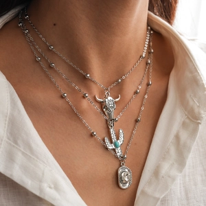 Detail of silver layered necklace featuring bull skull, cactus and cowboy hat charms