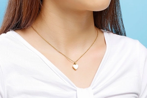 Détail d'un collier pendentif cœur doré minimaliste avec incrustation blanche sur un mannequin