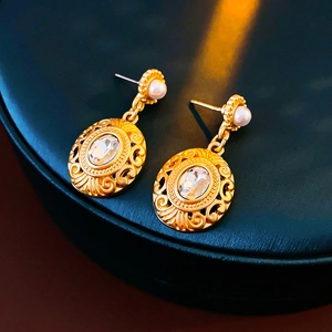 Macro detail of vintage gold earrings with engraved texture and clear gemstone