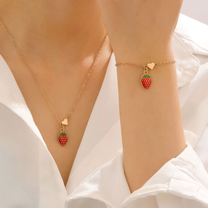 Dettaglio di fragole in smalto rosso e ciondoli a cuore dorati su collana e bracciale