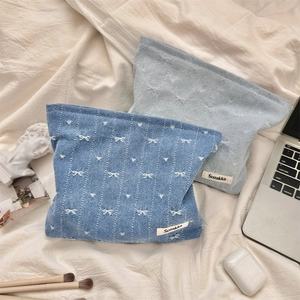 Detail of denim cosmetic bags with white bow embroidery in light and dark blue wash