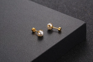 Detailed macro view of minimalist golden titanium steel earrings with white mini pearls