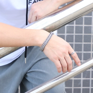 Close-up of a silver men's woven chain bracelet and matching ring on a model outdoors