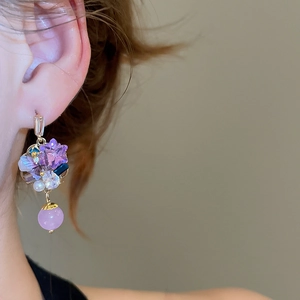 Close-up of Bohemian gold earrings with purple crystals and pearls worn by a model