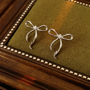 Gros plan de boucles d'oreilles nœuds argentés sur plateau en tissu vert foncé