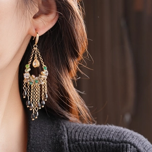 Detail of bohemian gold tassel earrings with green and black crystals on model