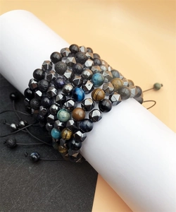 Detail of layered Tiger Eye and Hematite stone bracelets on a white cylinder stand