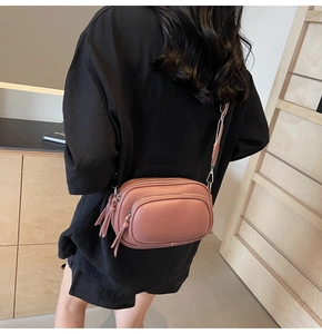 Detail of dusty pink crossbody bag featuring dual zippers and stylish tassel ornament