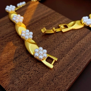 Detail of a vintage gold bracelet featuring white pearl flowers on a dark wood base