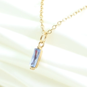 Golden necklace featuring a blue rectangular zircon pendant on a white fabric background