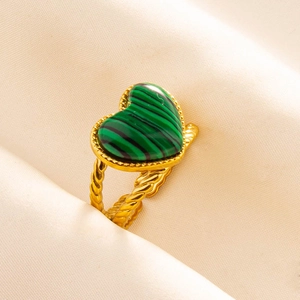 Close-up of green malachite heart ring with golden braided texture on beige fabric