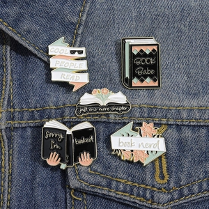 Detail view of five book-themed enamel pins styled on a blue denim jacket pocket