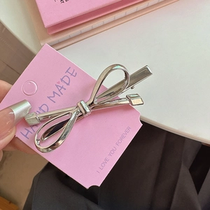 Elegant silver metal bow hair clip with polished finish on a pink gift card display