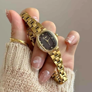 Elegant gold oval watch with black quilted dial and rhinestones worn over beige knitwear