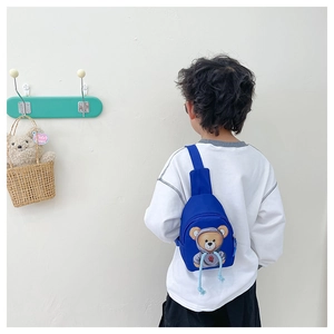 Detail view of a blue cartoon bear crossbody bag worn by a child in a studio setting