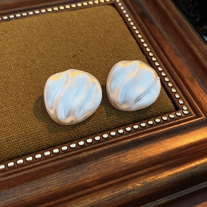 Close-up of white vintage geometric earrings with elegant swirl texture on green velvet