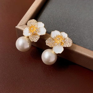 Macro detail of enamel flower earrings with sparkling zircons and a white pearl drop