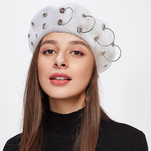 Close-up of white wool beret featuring decorative silver metal rings in punk style