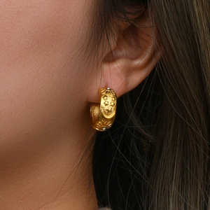 Macro detail of gold hoop earrings with celestial sun and moon relief patterns and zircons