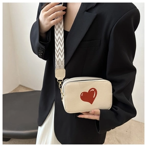 Detail of cream leather crossbody bag with red heart print and wide patterned strap