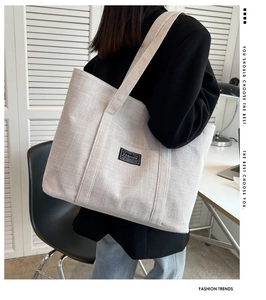 Detail view of off-white canvas tote bag featuring a black FASHION woven label