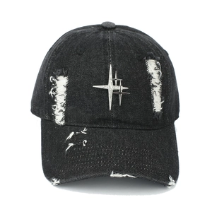 Close-up of a distressed black denim baseball cap with silver metal star and rivets detail