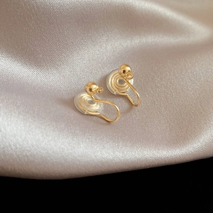 Detail of gold clip-on earrings with soft silicone pads on a champagne silk fabric
