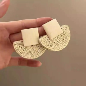 Detail of bohemian rattan earrings with beige square studs and woven semi-circle pendants