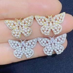 Macro detail of butterfly stud earrings featuring pearls and sparkling cubic zirconia stones