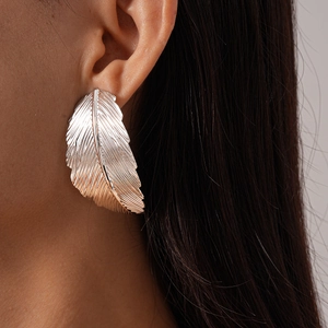 Close-up of a silver leaf-shaped statement earring with detailed metallic texture on model