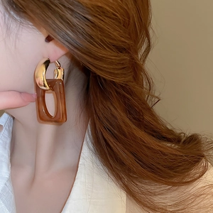 Close-up of model wearing geometric gold hoop earrings with amber resin pendant drops